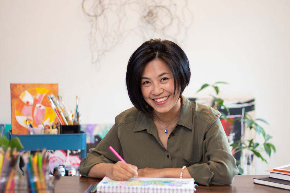 Portrait of Jeni Chen, drawing at her table holding a pencil